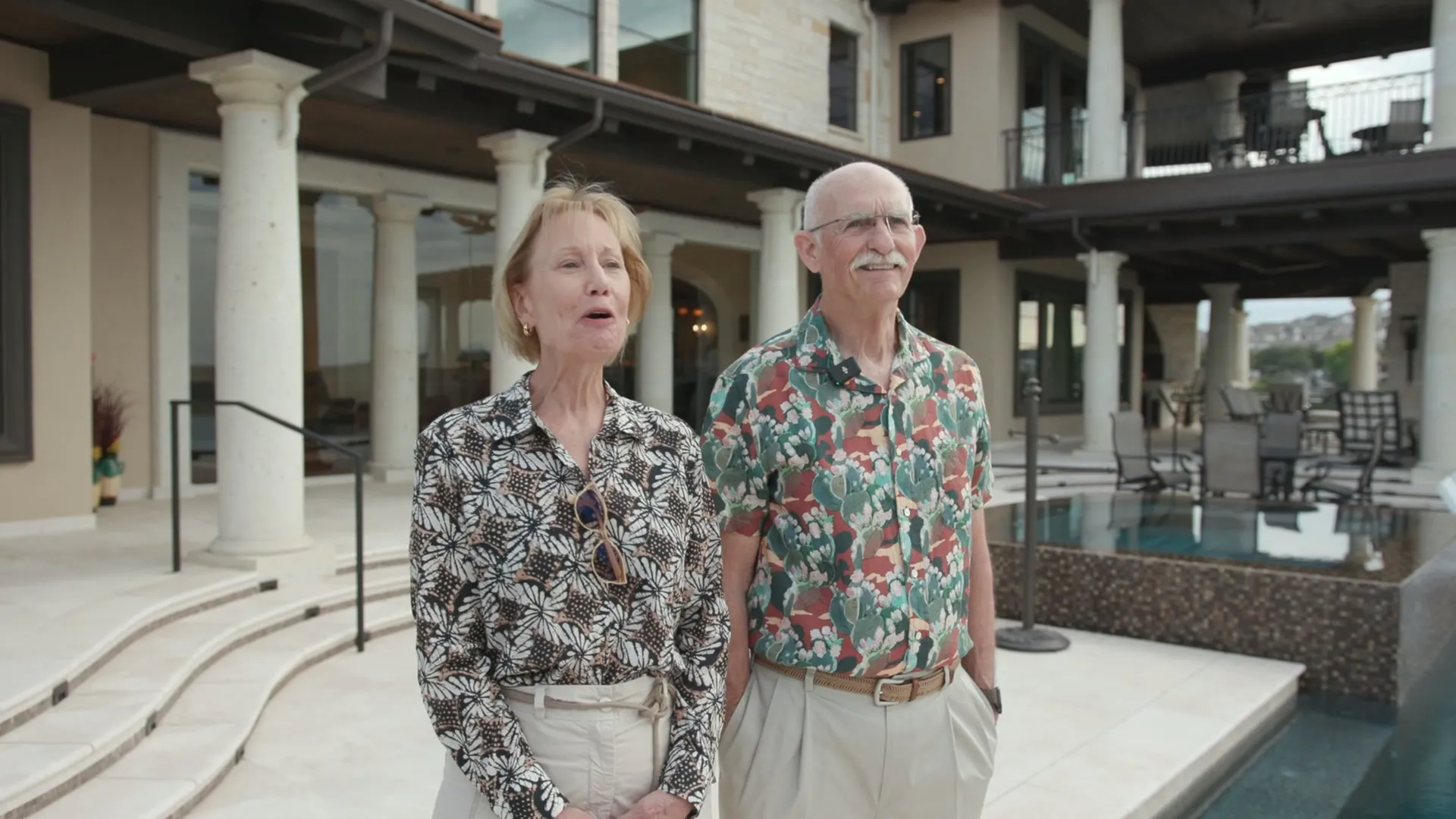 A couple standing together on a stone terrace beside a pool