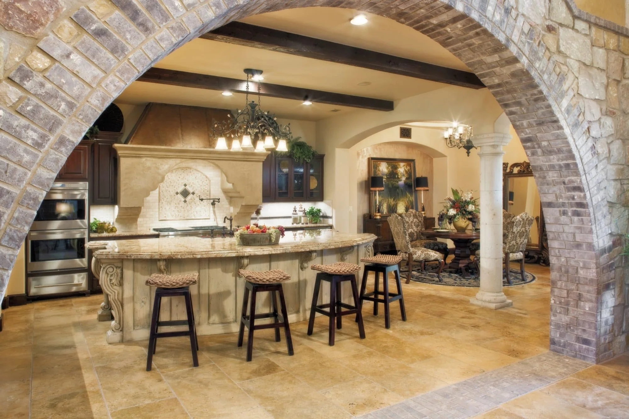Kitchen seen through a stone and brick arch with curved island and barstools, Mediterranean Parade Home