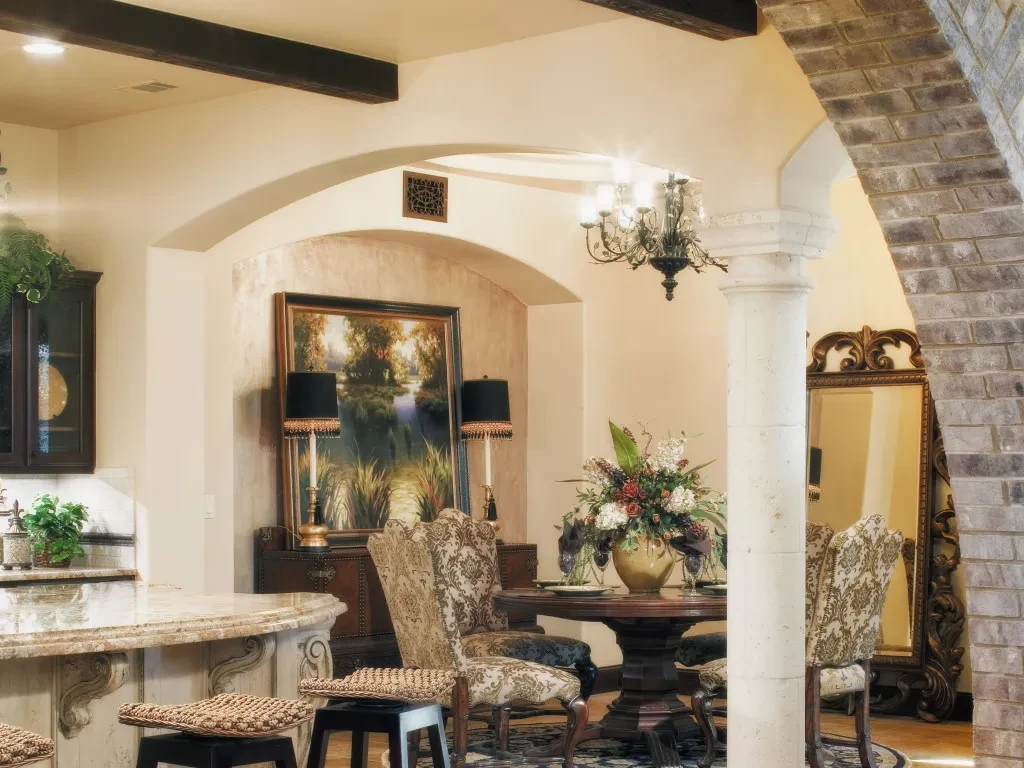 Dining alcove with landscape painting beside the kitchen island, past a brick arch, Mediterranean Parade Home