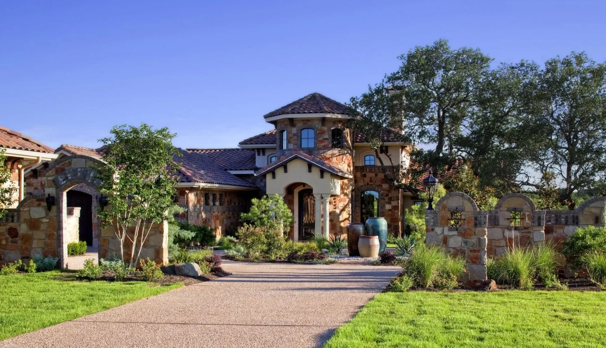 Front entry with stone tower, tile roof and walled courtyard gate, Mediterranean Parade Home