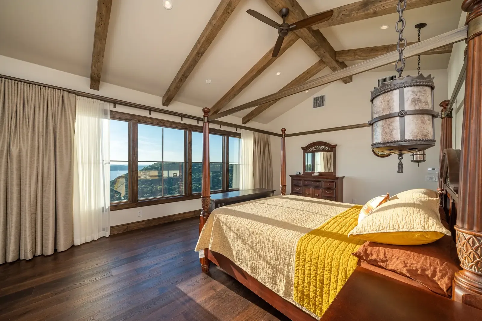 Luxury primary suite bedroom with vaulted beamed ceiling and panoramic views