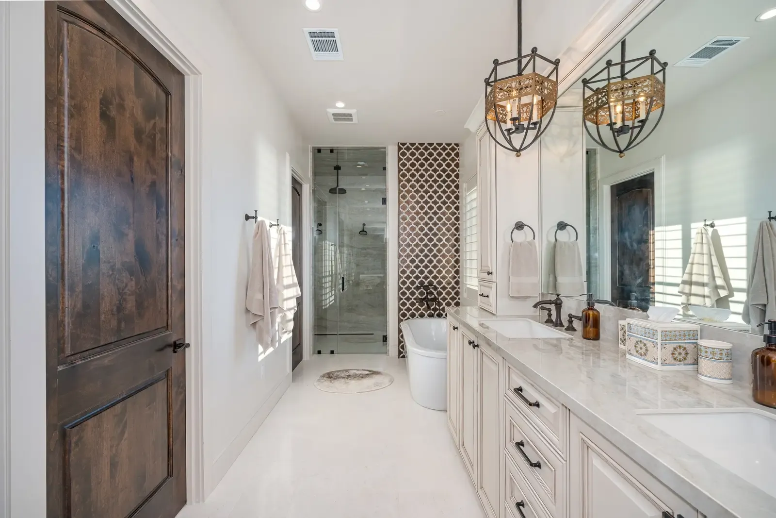 Spacious luxury primary suite bathroom with dual vanities and patterned accent tile