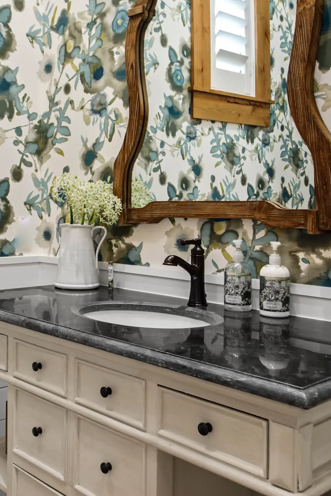 Bathroom vanity with floral wallpaper and vintage wood mirror