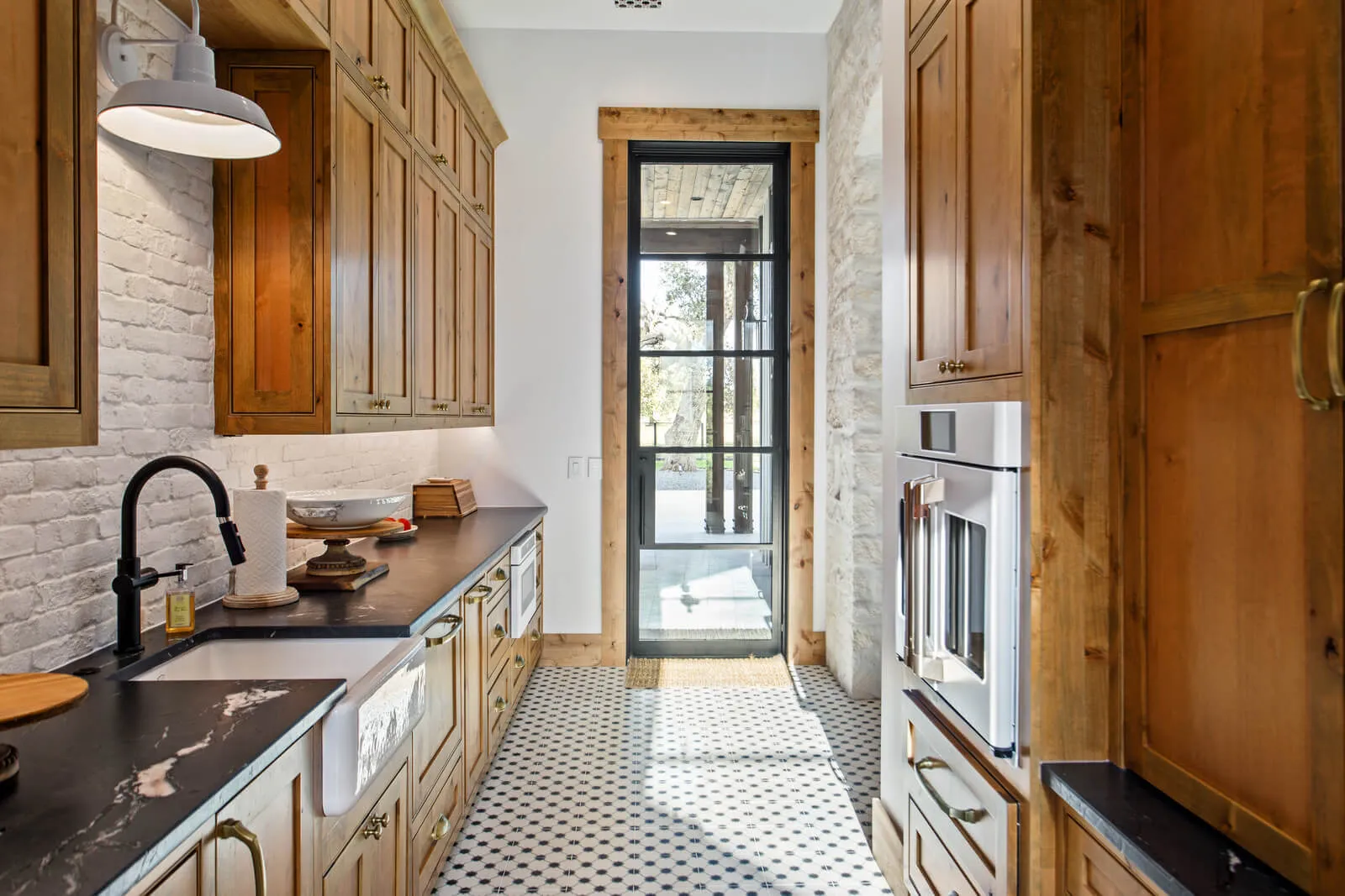 Warm wood scullery kitchen with farmhouse sink, patterned tile floors, and hidden appliance storage