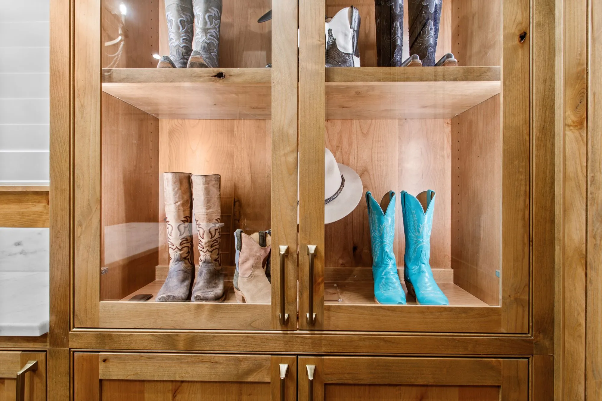 Lit glass-front cabinet displaying cowboy boots and a hat in a Jenkins Design Build custom home