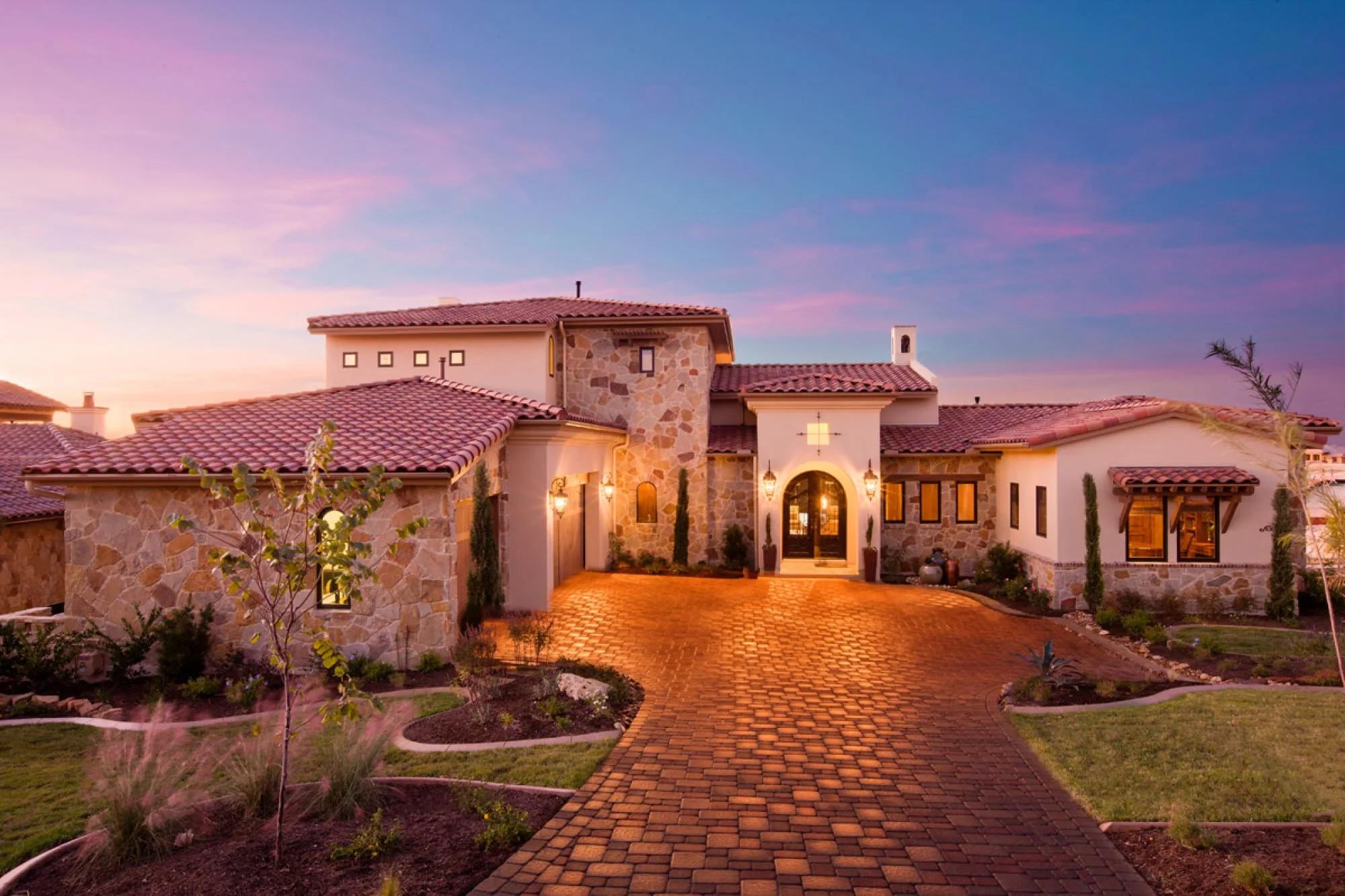 Stone and stucco front of the home with tile roof and paver drive at dusk, Modern Mediterranean Parade Home