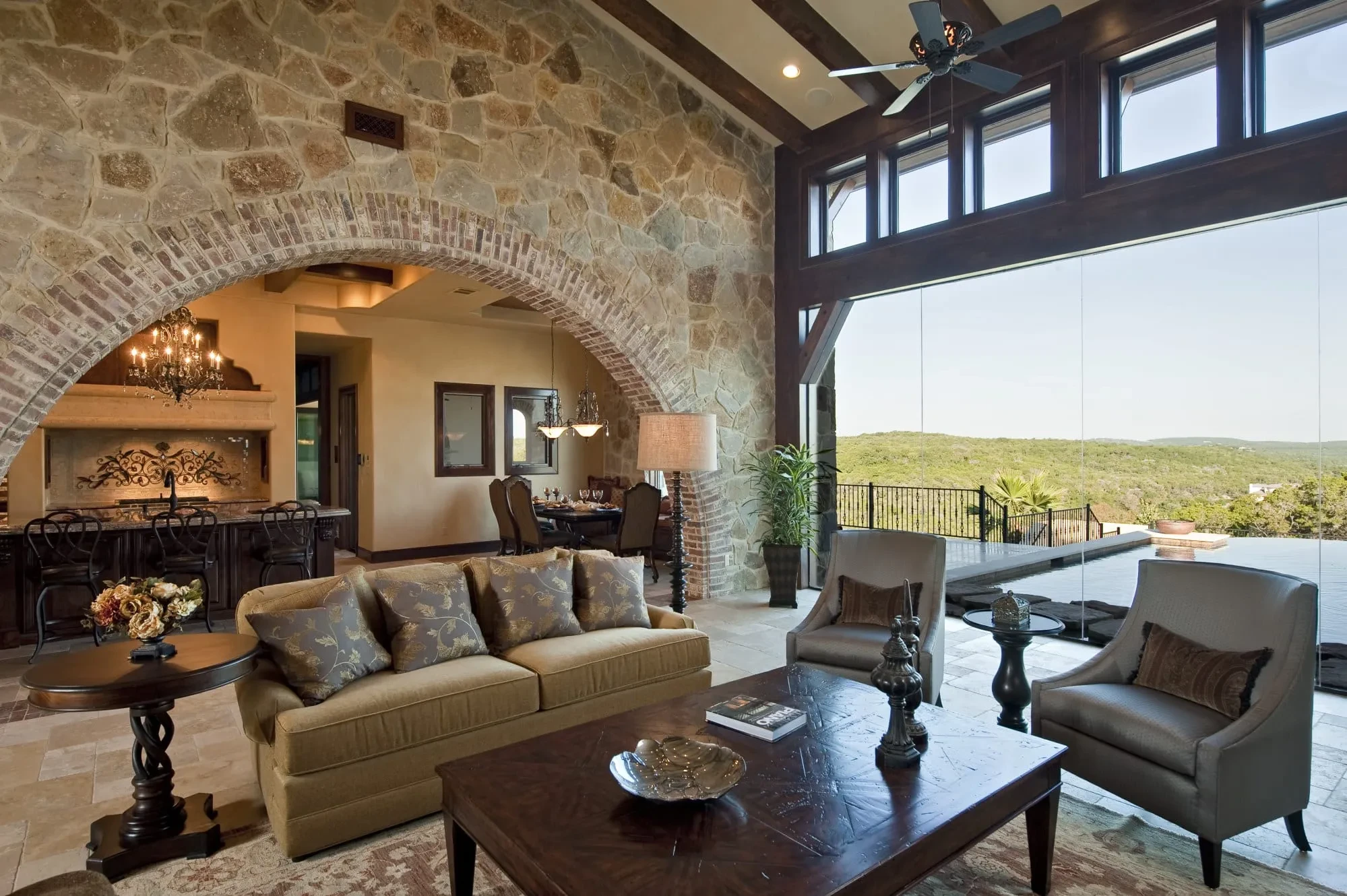 Great room with stone arch, beamed ceiling and glass wall open to the pool and hills, Modern Mediterranean Parade Home