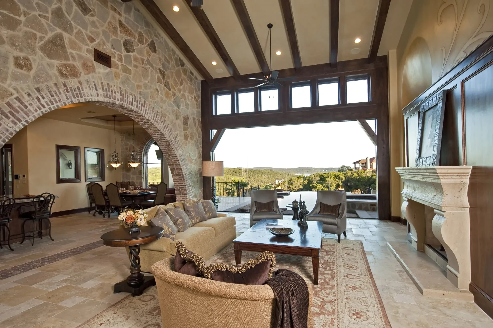 Great room with carved stone fireplace mantel and glass wall opening to the hills, Modern Mediterranean Parade Home