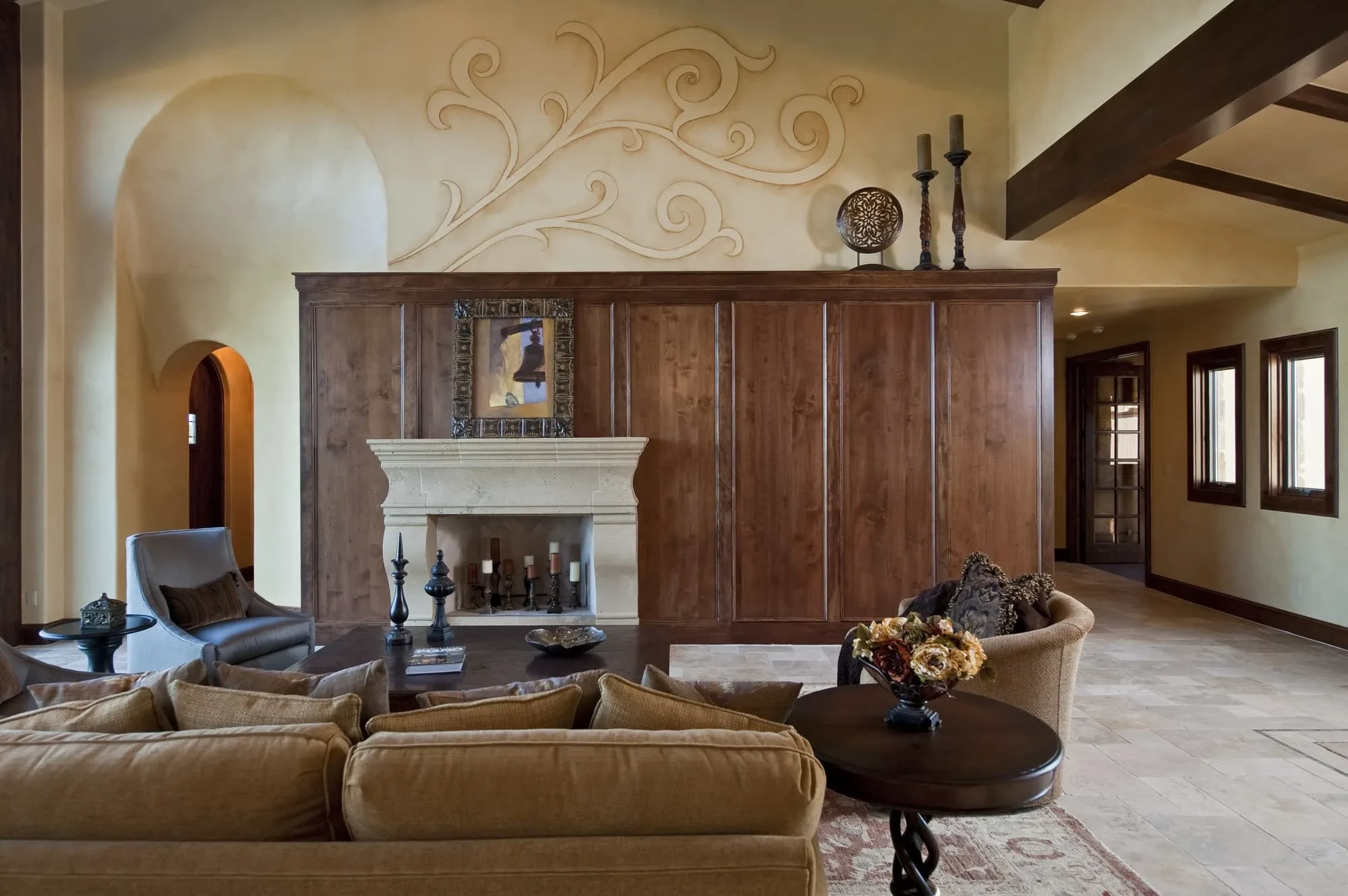Fireplace wall with closed wood-paneled cabinetry, limestone mantel and plaster scroll above, Modern Mediterranean Parade Home
