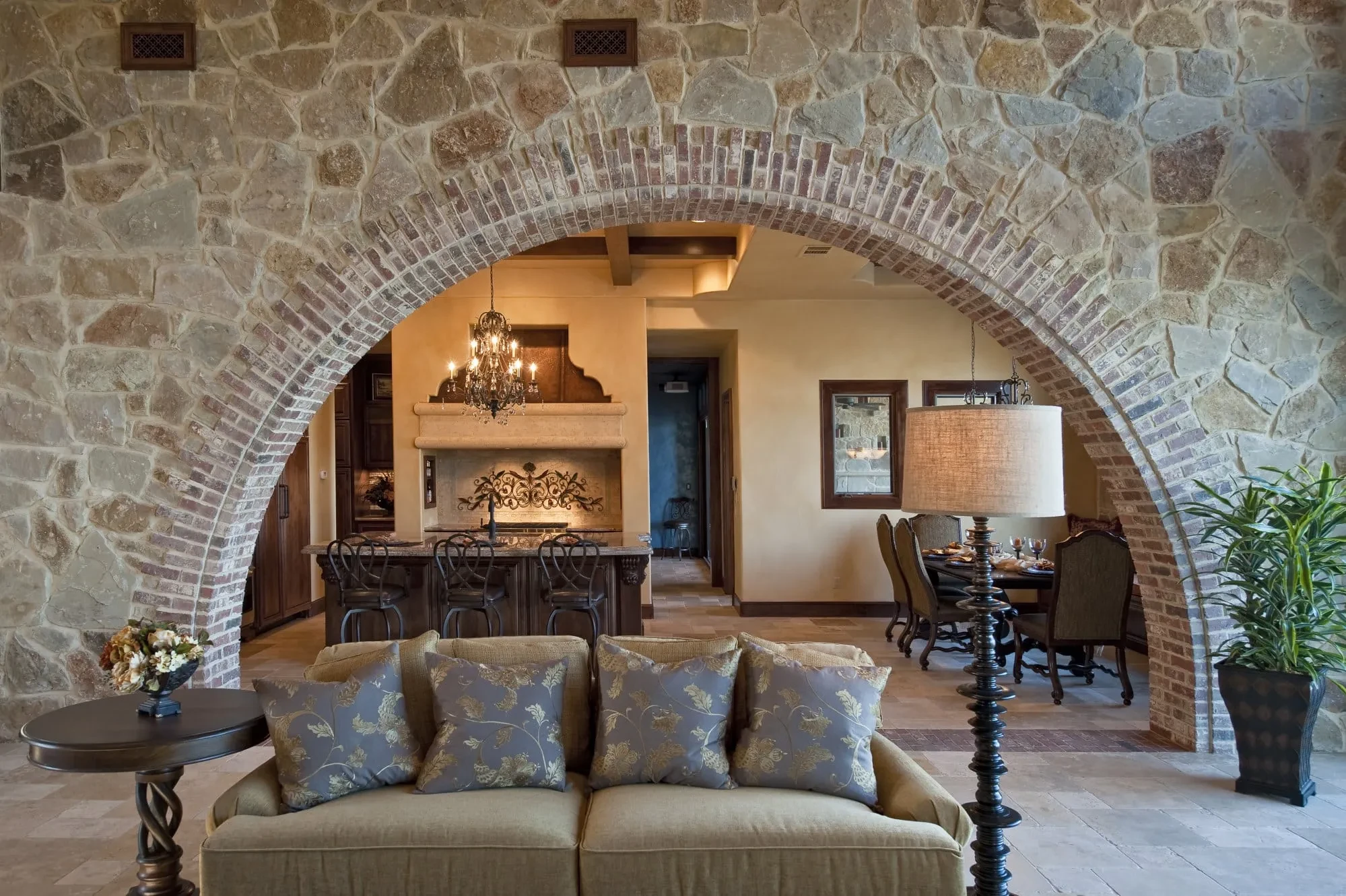 Sofa in front of a stone and brick arch framing the kitchen and dining room, Modern Mediterranean Parade Home