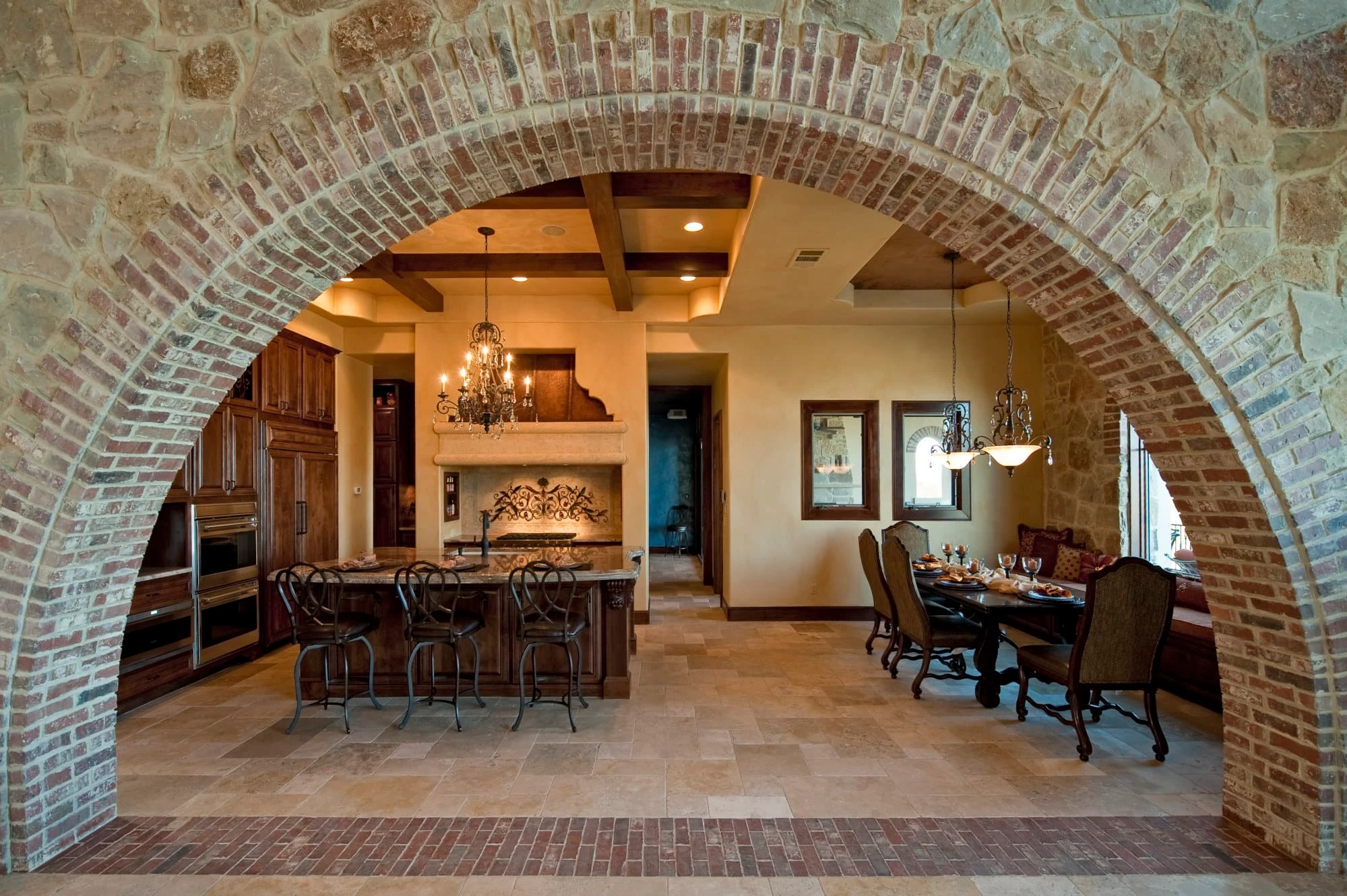 Wide view through a brick arch to the kitchen island, dining table and brick floor border, Modern Mediterranean Parade Home