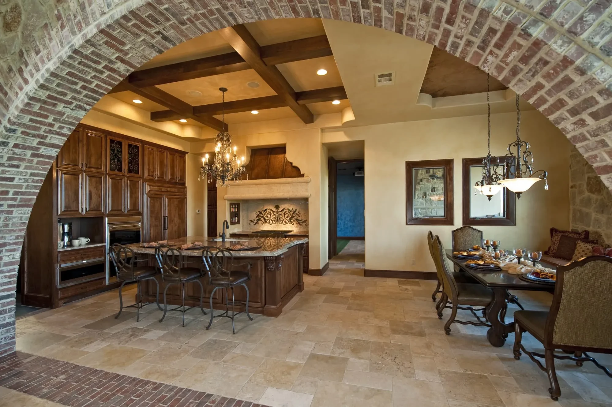 Close view through a brick arch of coffered beam ceiling, kitchen island and dining table, Modern Mediterranean Parade Home