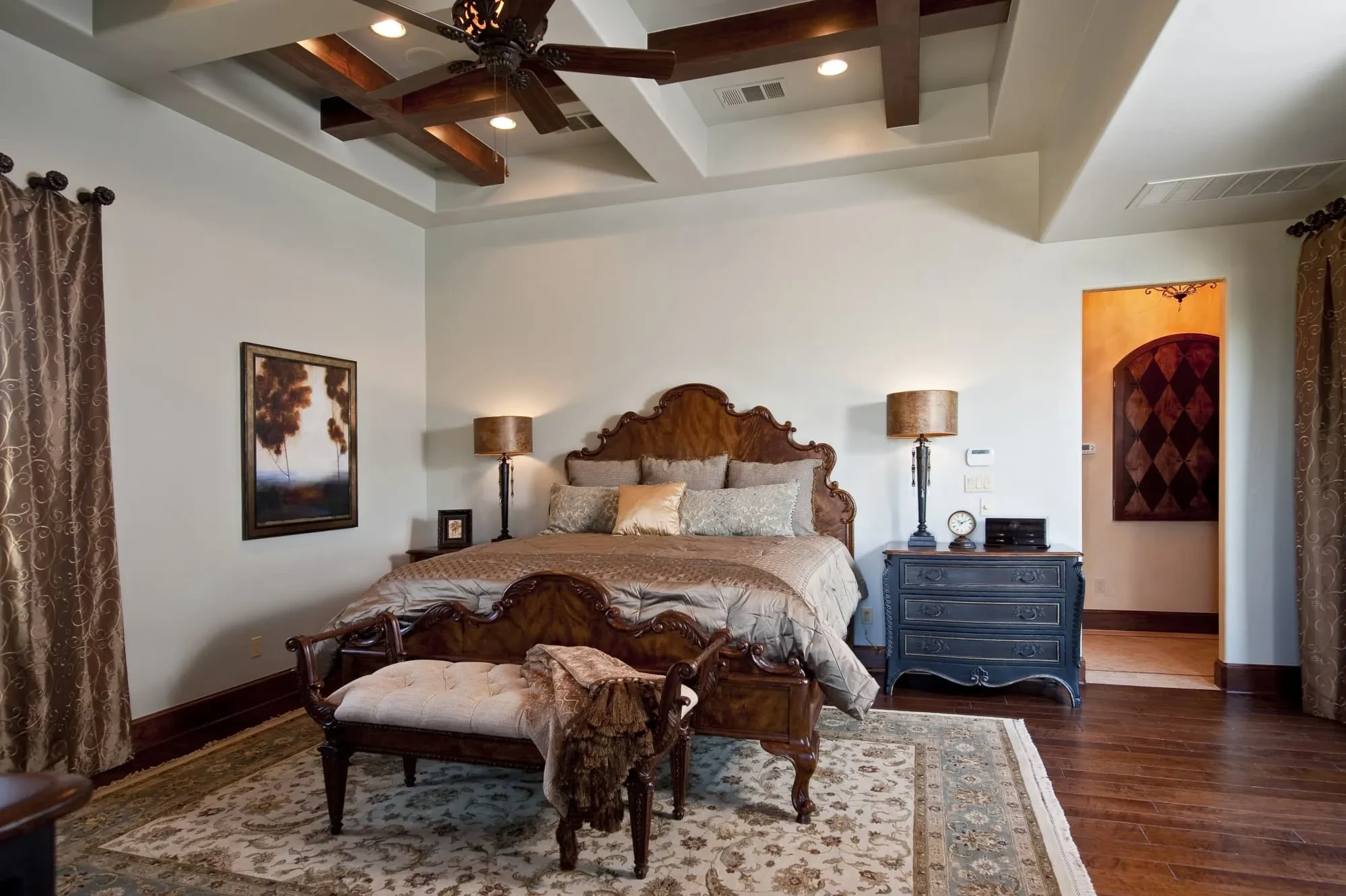 Bedroom with carved wood bed, upholstered bench and coffered beam ceiling, Modern Mediterranean Parade Home