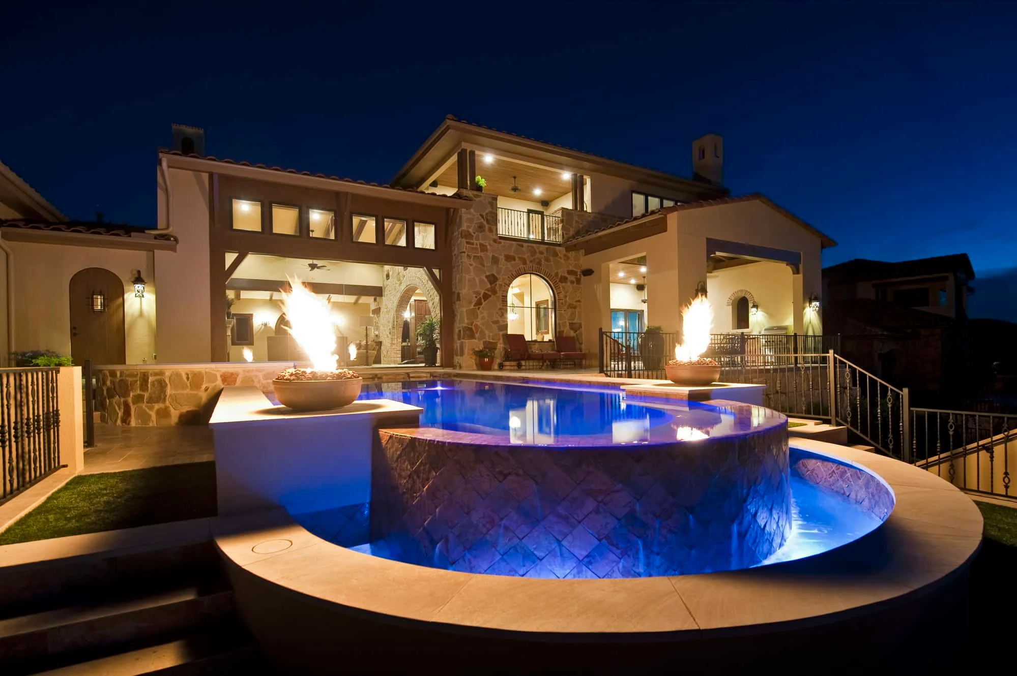 Raised spa and pool with two fire bowls lit at night, the house behind, Modern Mediterranean Parade Home