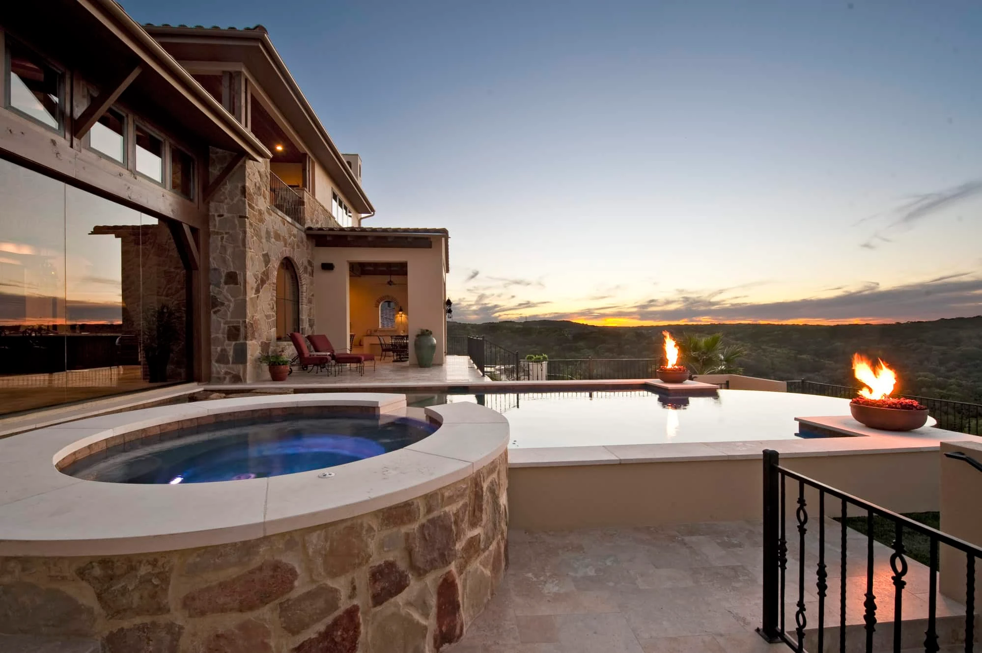 Stone-clad round spa, vanishing-edge pool and fire bowls at dusk, Modern Mediterranean Parade Home