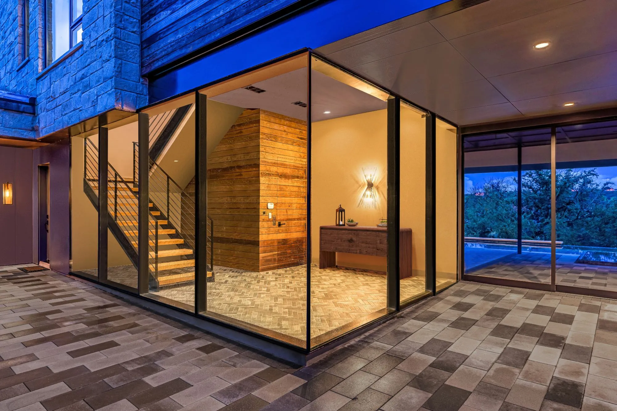 Glass-walled entry with a floating stair and wood-clad wall, lit at dusk
