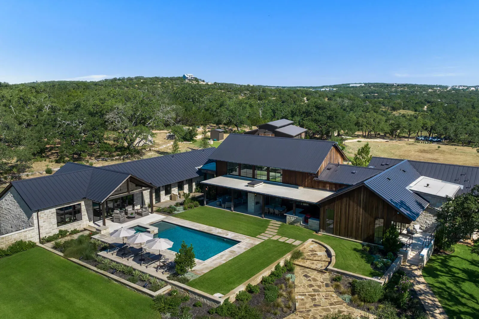 Aerial view of Hill Country estate in Austin with metal roof, wood siding, and pool