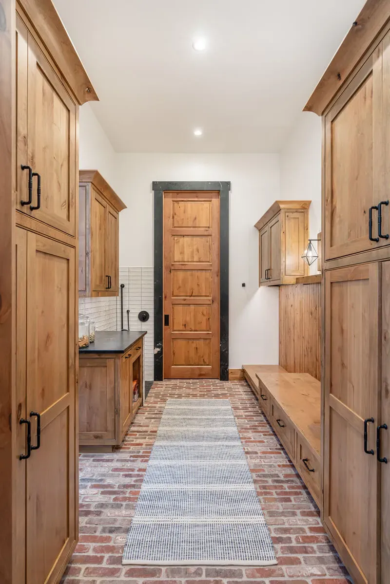 Long mudroom corridor with cabinets, bench, and tile splash.