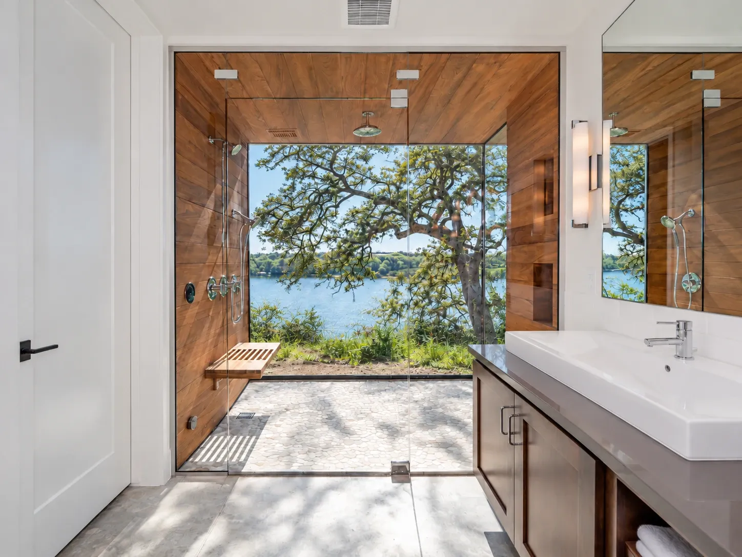 Walk-in shower with a glass wall looking out through an oak tree to the lake