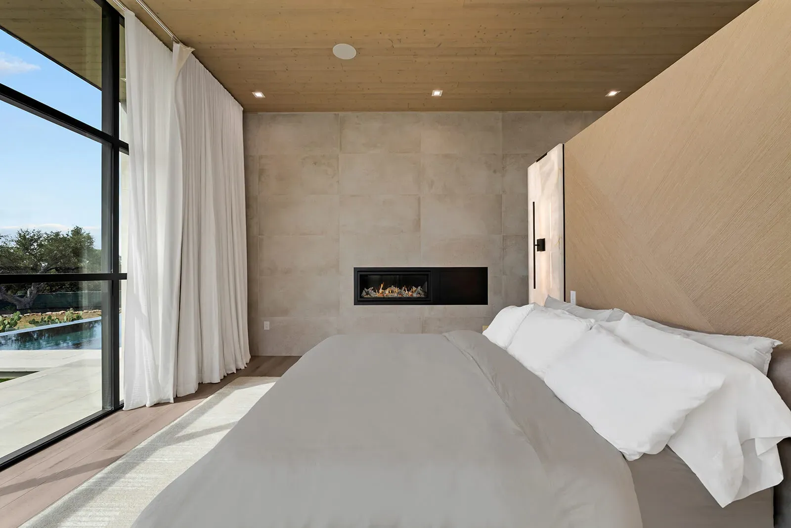 Minimalist luxury bedroom with modern fireplace and large window overlooking pool