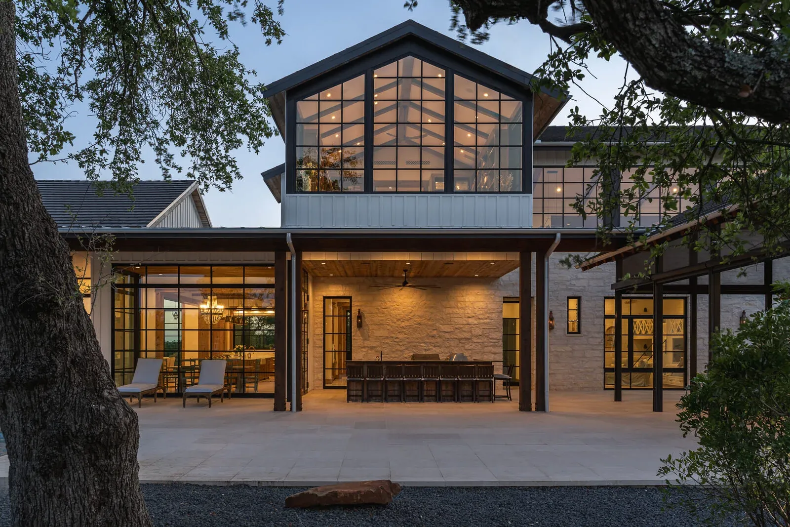Modern farmhouse front exterior at dusk with large windows and warm lighting
