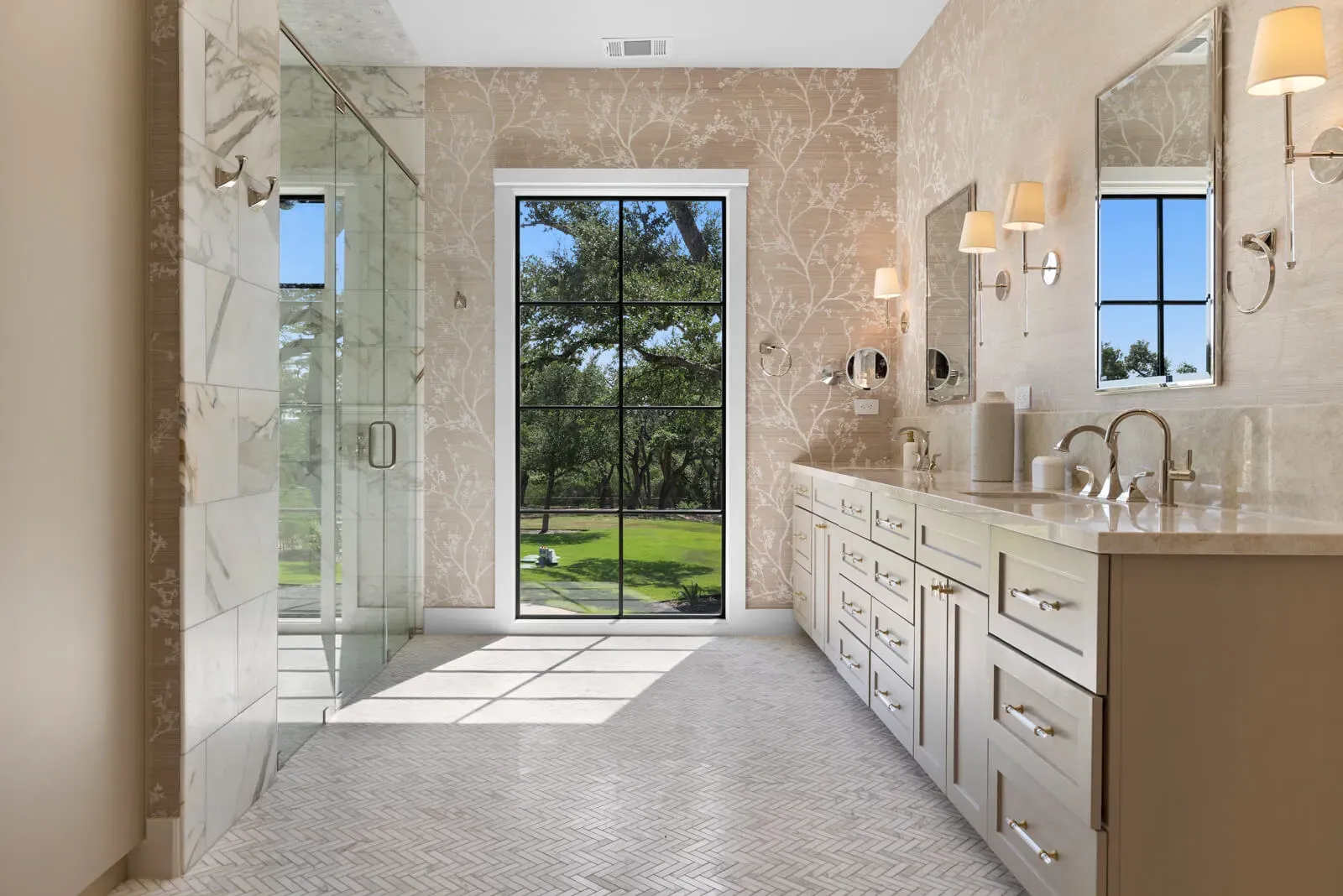 Marble walk-in shower with herringbone floor tile and curbless entry designed for aging in place in a luxury Austin custom home