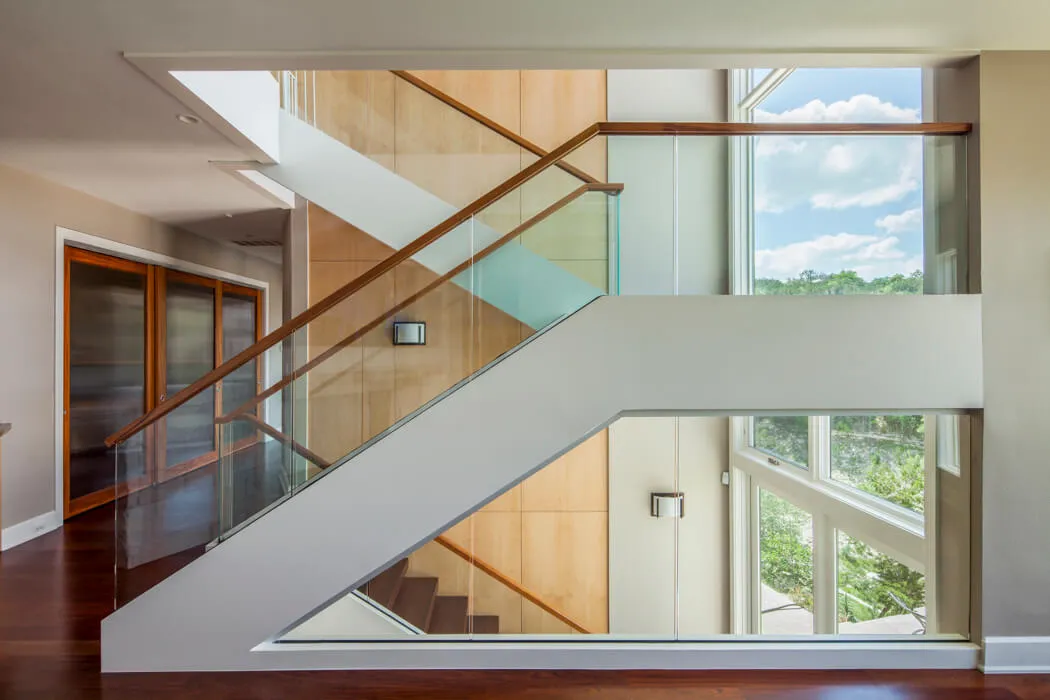 A custom mixed-media staircase with steel stringers, warm wood treads, and a glass balustrade in a modern Austin home.