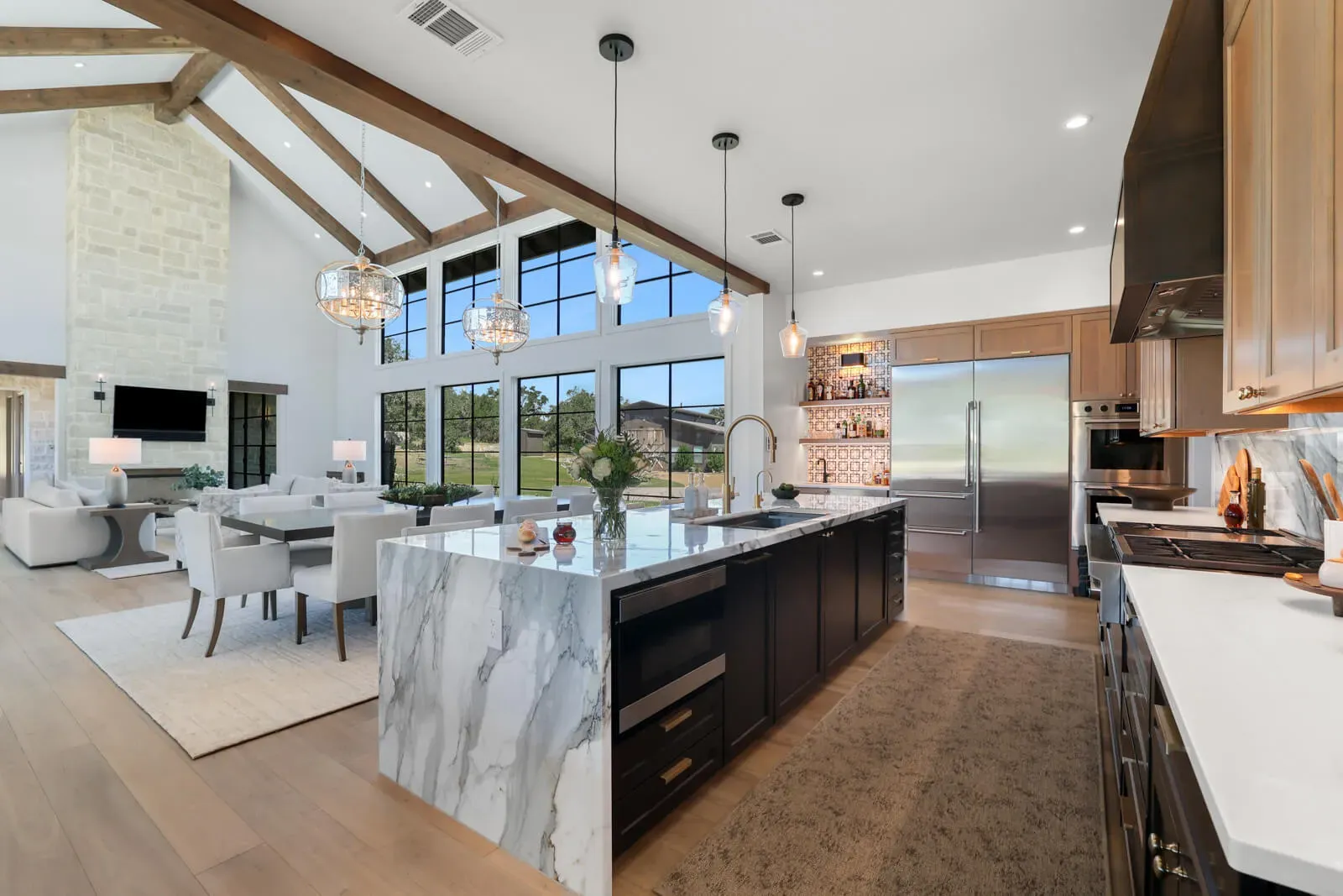 Open-concept main kitchen and great room with vaulted beams and large windows.
