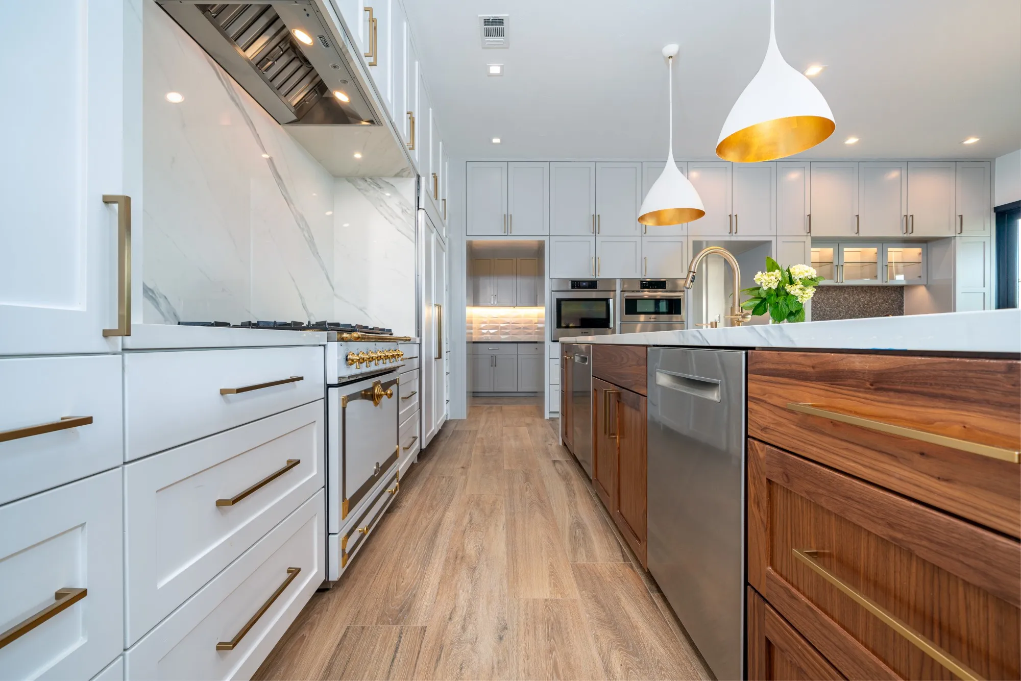 White and walnut kitchen with brass pulls, a French range and gold-lined pendants